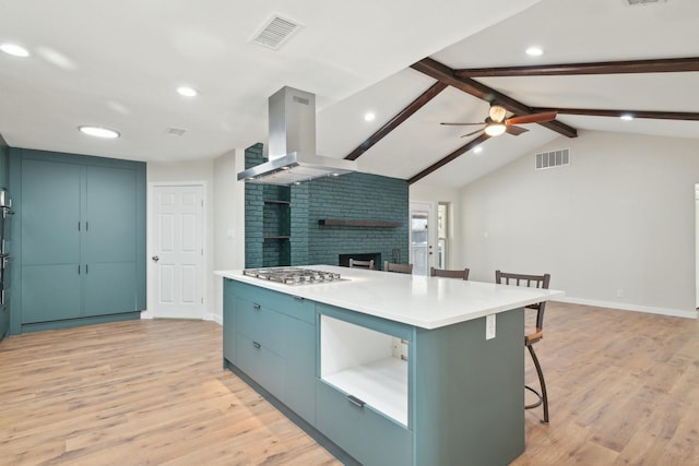 kitchen with vaulted ceiling with beams, island range hood, a breakfast bar, visible vents, and a brick fireplace