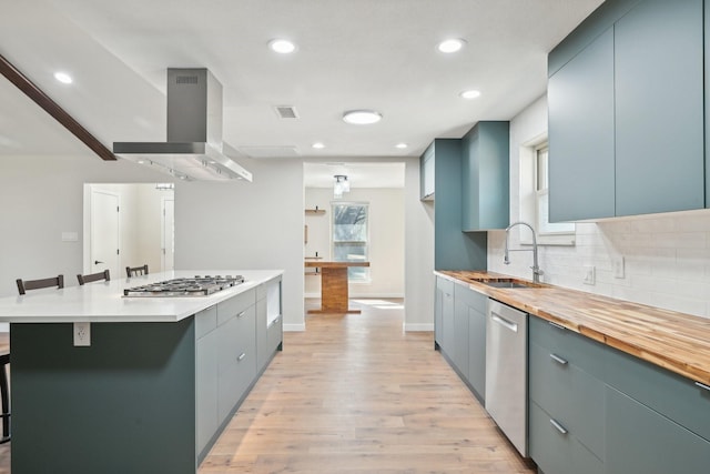 kitchen featuring light wood-style flooring, island range hood, a sink, appliances with stainless steel finishes, and decorative backsplash