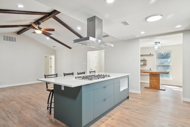 kitchen with visible vents, island range hood, vaulted ceiling with beams, a kitchen bar, and stainless steel gas cooktop