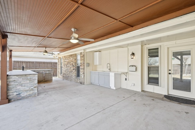 view of patio featuring a sink, ceiling fan, fence, and exterior kitchen