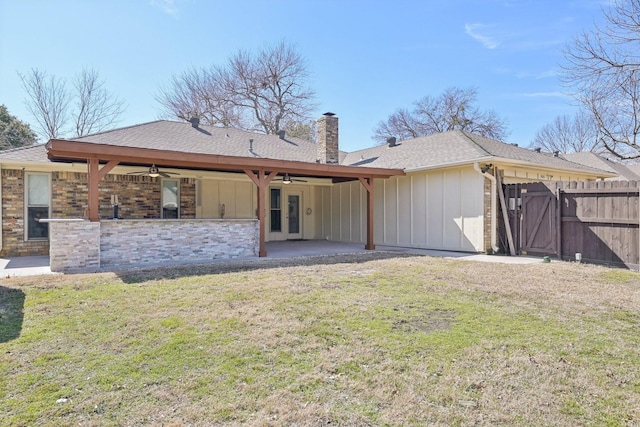 rear view of house with a ceiling fan, a patio, a chimney, a yard, and board and batten siding