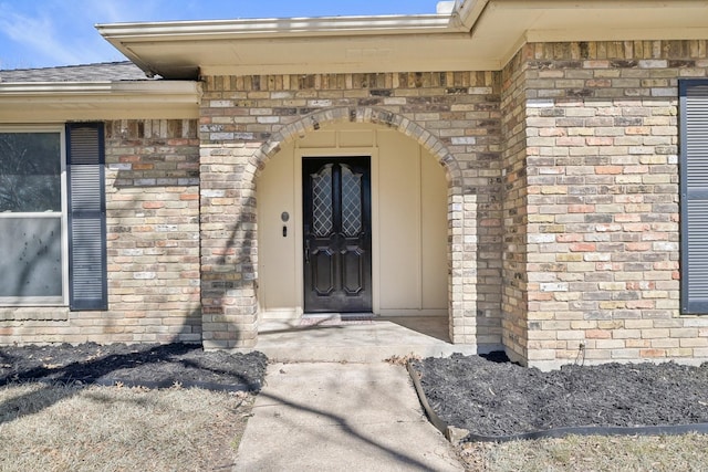 entrance to property with roof with shingles and brick siding