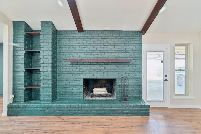 unfurnished living room featuring vaulted ceiling with beams, a brick fireplace, wood finished floors, and baseboards