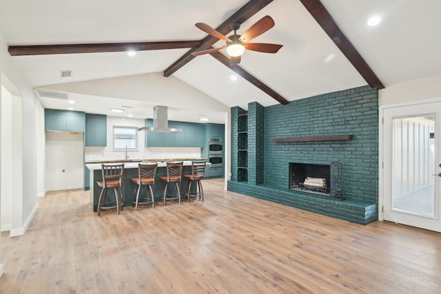 kitchen with lofted ceiling with beams, light wood-style flooring, a breakfast bar area, ventilation hood, and a brick fireplace