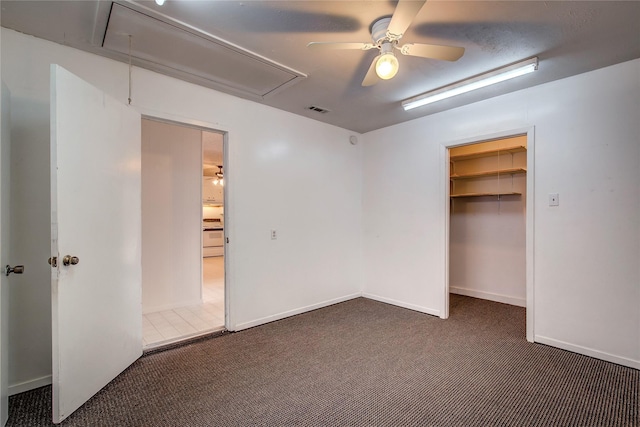 unfurnished bedroom featuring a walk in closet, dark colored carpet, visible vents, attic access, and ceiling fan