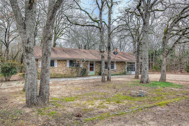 ranch-style home featuring dirt driveway, a chimney, and brick siding