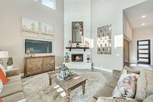 living area with recessed lighting, a high ceiling, a stone fireplace, wood finished floors, and baseboards