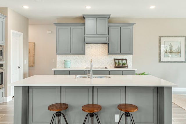 kitchen featuring tasteful backsplash, stainless steel appliances, gray cabinets, light countertops, and a sink