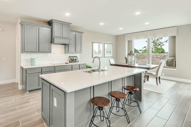 kitchen featuring light countertops, a sink, backsplash, and gray cabinetry