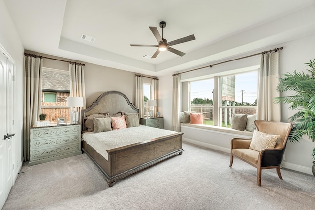 carpeted bedroom featuring a ceiling fan, visible vents, a tray ceiling, and baseboards