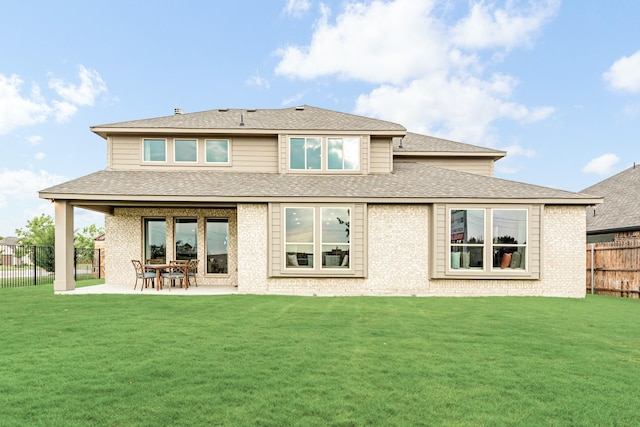 rear view of house featuring a patio, a fenced backyard, a shingled roof, brick siding, and a yard