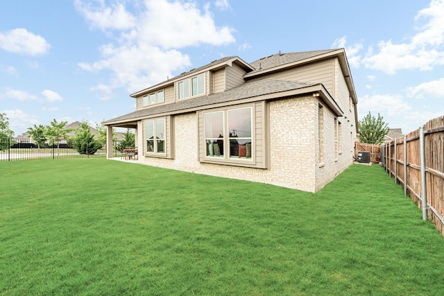 back of property with brick siding, a fenced backyard, roof with shingles, and a yard