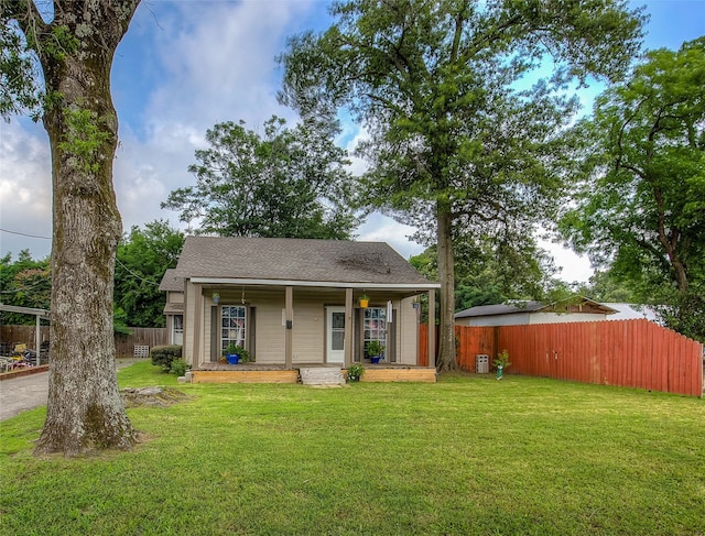 view of front of property with covered porch, fence, a front lawn, and roof with shingles