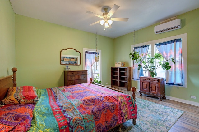 bedroom featuring an AC wall unit, multiple windows, baseboards, and wood finished floors