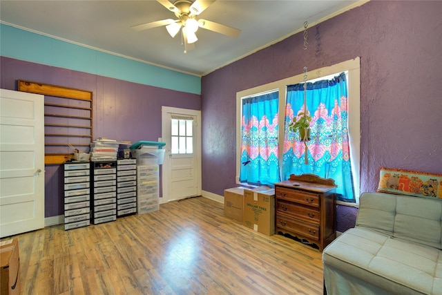 living area with crown molding, ceiling fan, wood finished floors, and a textured wall