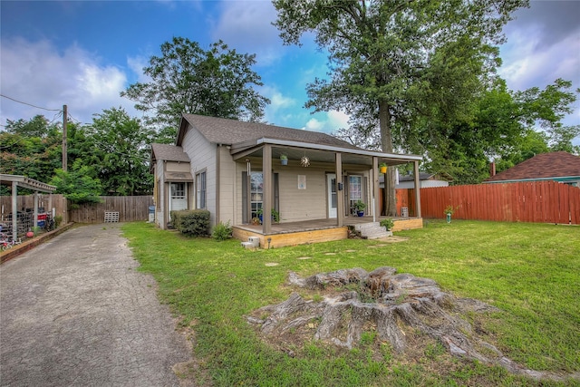 view of front facade with aphalt driveway, a shingled roof, covered porch, a front yard, and fence