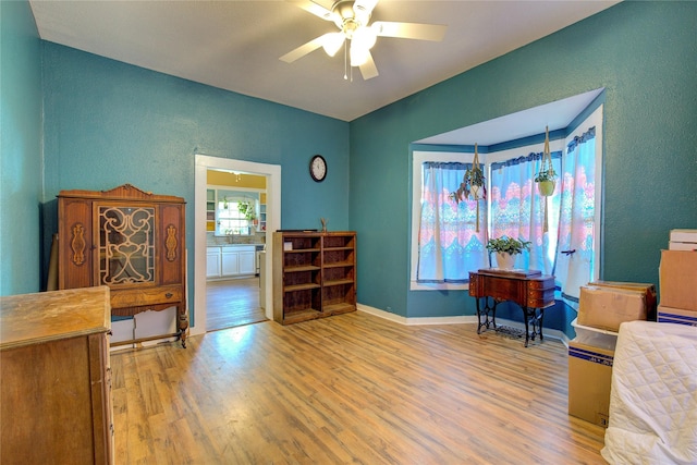 sitting room with ceiling fan, a textured wall, wood finished floors, and baseboards