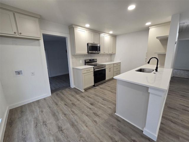 kitchen with appliances with stainless steel finishes, light wood-type flooring, a sink, and tasteful backsplash