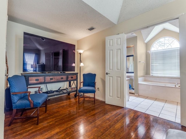 sitting room with visible vents, a textured ceiling, wood-type flooring, and lofted ceiling