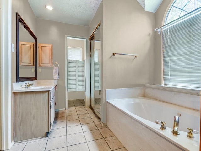 bathroom featuring a textured ceiling, tile patterned floors, a garden tub, and vanity