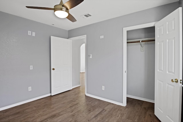 unfurnished bedroom featuring arched walkways, a closet, wood finished floors, and baseboards