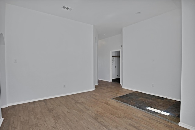 empty room featuring baseboards, visible vents, arched walkways, and wood finished floors