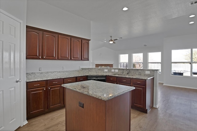 kitchen with a peninsula, a sink, black dishwasher, light wood-type flooring, and a center island