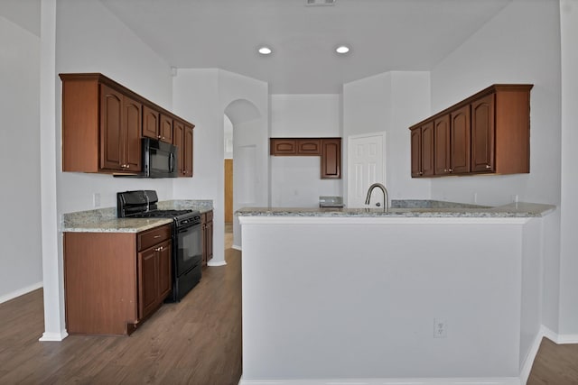 kitchen featuring arched walkways, wood finished floors, light stone countertops, a peninsula, and black appliances