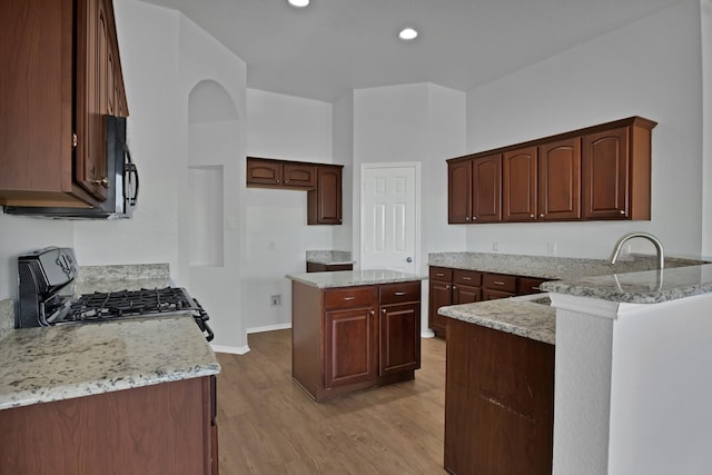 kitchen with light stone counters, light wood finished floors, gas range oven, recessed lighting, and black microwave