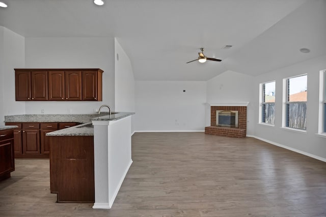 kitchen with visible vents, a ceiling fan, lofted ceiling, a fireplace, and a sink