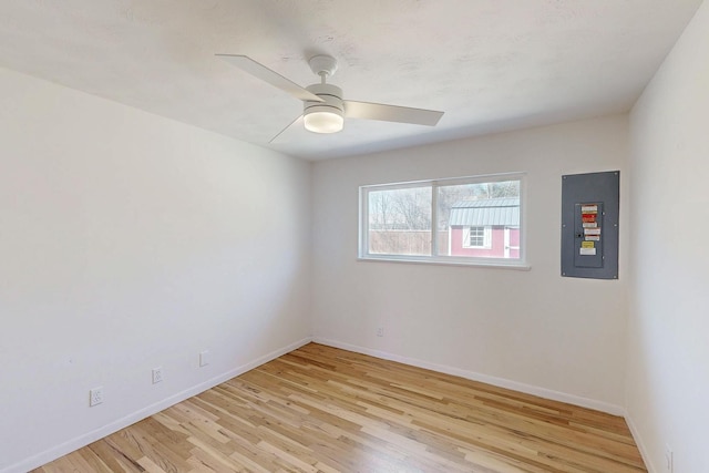 empty room with light wood-type flooring, electric panel, ceiling fan, and baseboards