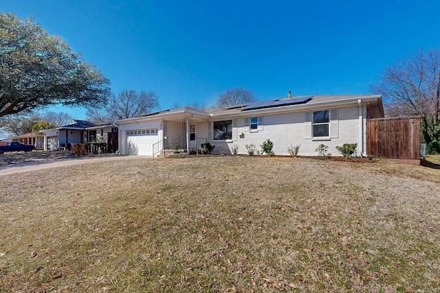 ranch-style home featuring an attached garage, brick siding, driveway, roof mounted solar panels, and a front yard