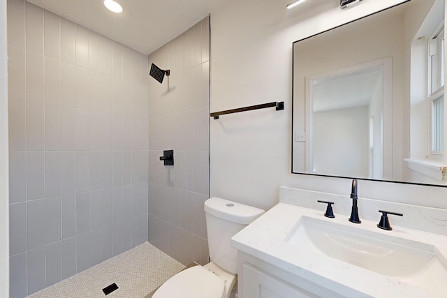 bathroom with toilet, a tile shower, and vanity