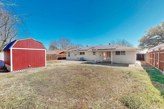 rear view of property with an outbuilding, solar panels, a lawn, a patio area, and a fenced backyard