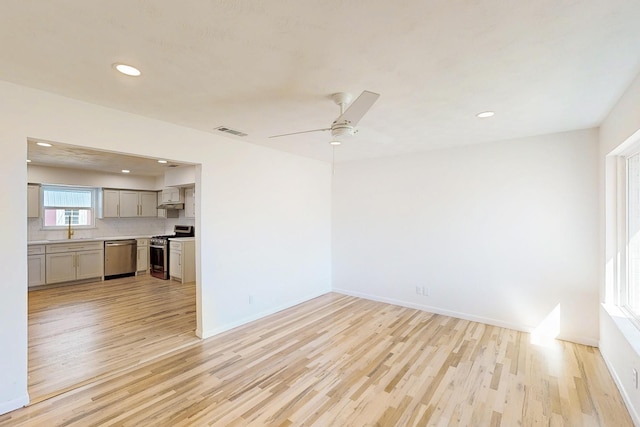 unfurnished room featuring light wood-style flooring, a sink, visible vents, and baseboards