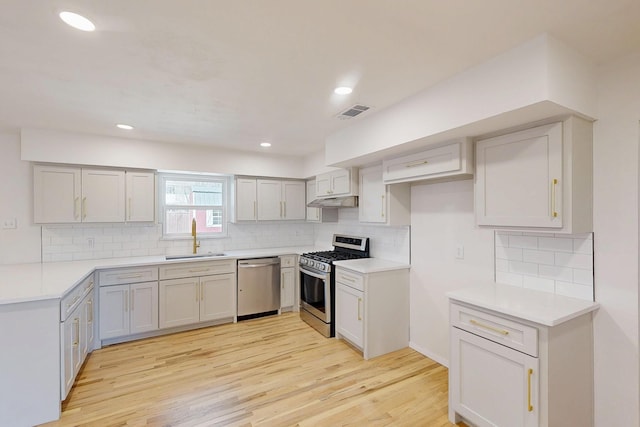 kitchen featuring backsplash, appliances with stainless steel finishes, a sink, light wood-type flooring, and under cabinet range hood