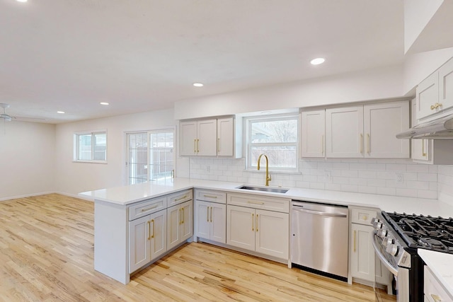 kitchen with appliances with stainless steel finishes, a sink, a peninsula, and light wood finished floors