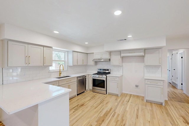 kitchen with stainless steel appliances, light countertops, light wood-style floors, a sink, and a peninsula