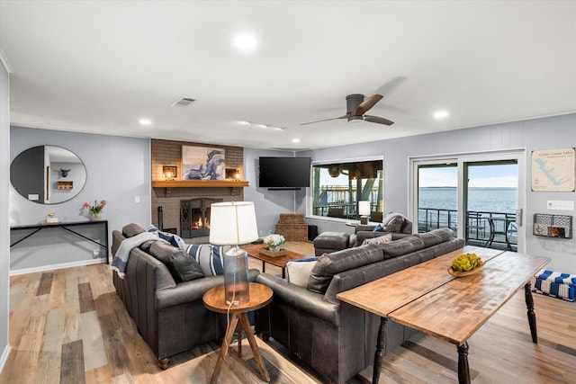 living area with recessed lighting, visible vents, a ceiling fan, a brick fireplace, and light wood-type flooring