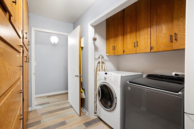 clothes washing area featuring light wood finished floors, washing machine and clothes dryer, cabinet space, and baseboards