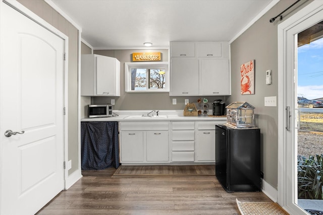 kitchen with wood finished floors, a sink, white cabinets, light countertops, and stainless steel microwave