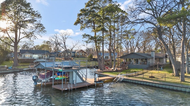 view of dock with boat lift, a water view, fence, a lawn, and a residential view