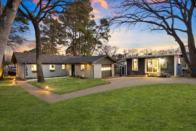 back of house at dusk with a garage, aphalt driveway, a lawn, and brick siding