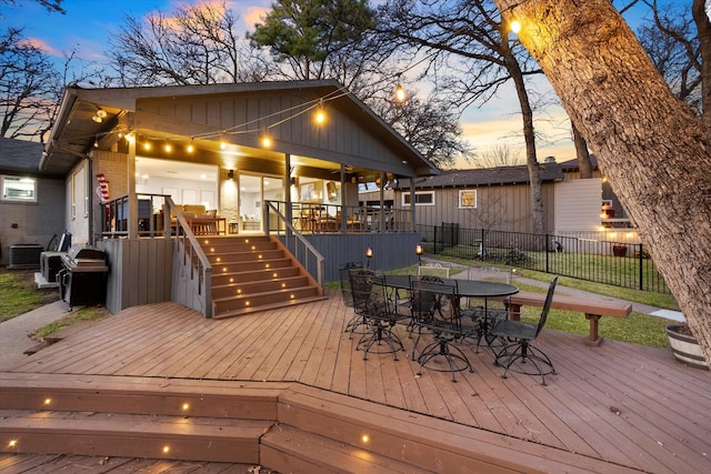 deck at dusk with fence, outdoor dining area, and central AC