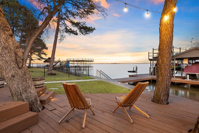 view of dock featuring a water view, boat lift, fence, and a yard