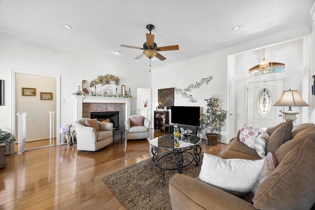 living room with a tiled fireplace, a ceiling fan, wood finished floors, crown molding, and recessed lighting