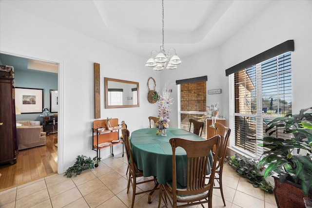 dining space featuring a raised ceiling, a notable chandelier, and light tile patterned floors