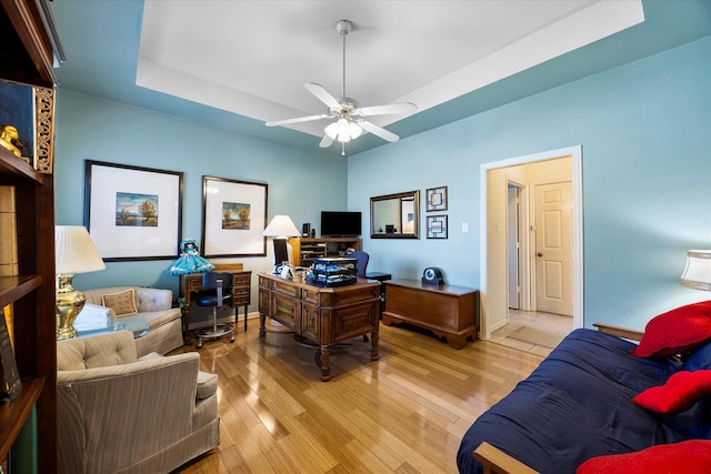 office space with light wood-style floors, baseboards, a raised ceiling, and a ceiling fan