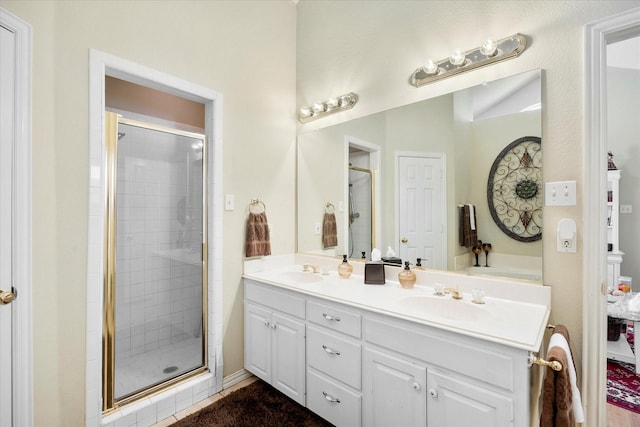 full bath featuring double vanity, a sink, and a shower stall