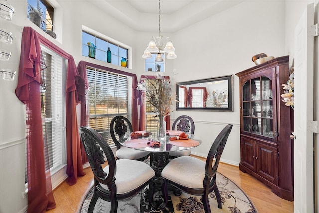 dining space with light wood-type flooring, a towering ceiling, baseboards, and a notable chandelier